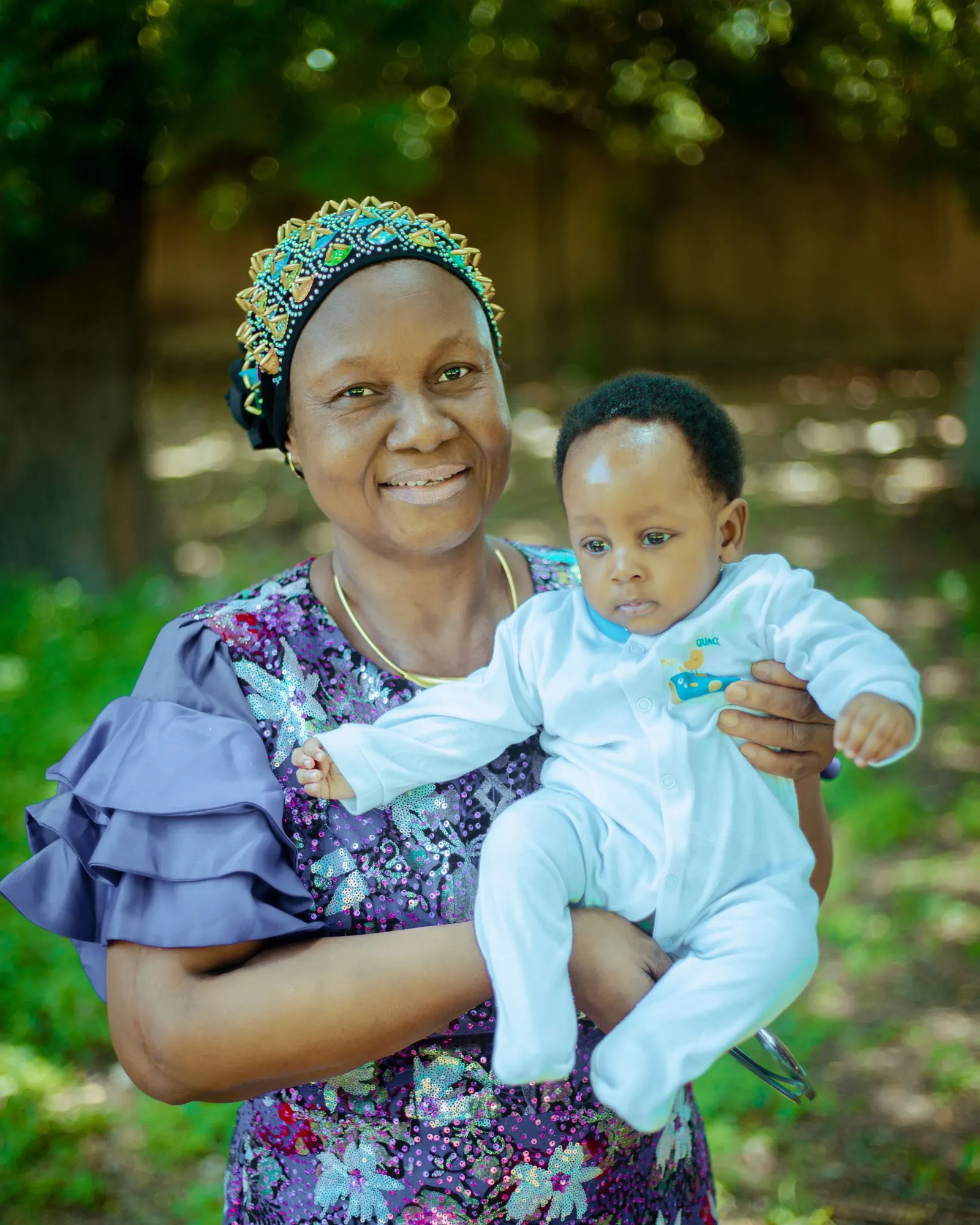 Smiling grandmother in a beaded headpiece holding her baby grandson outdoors